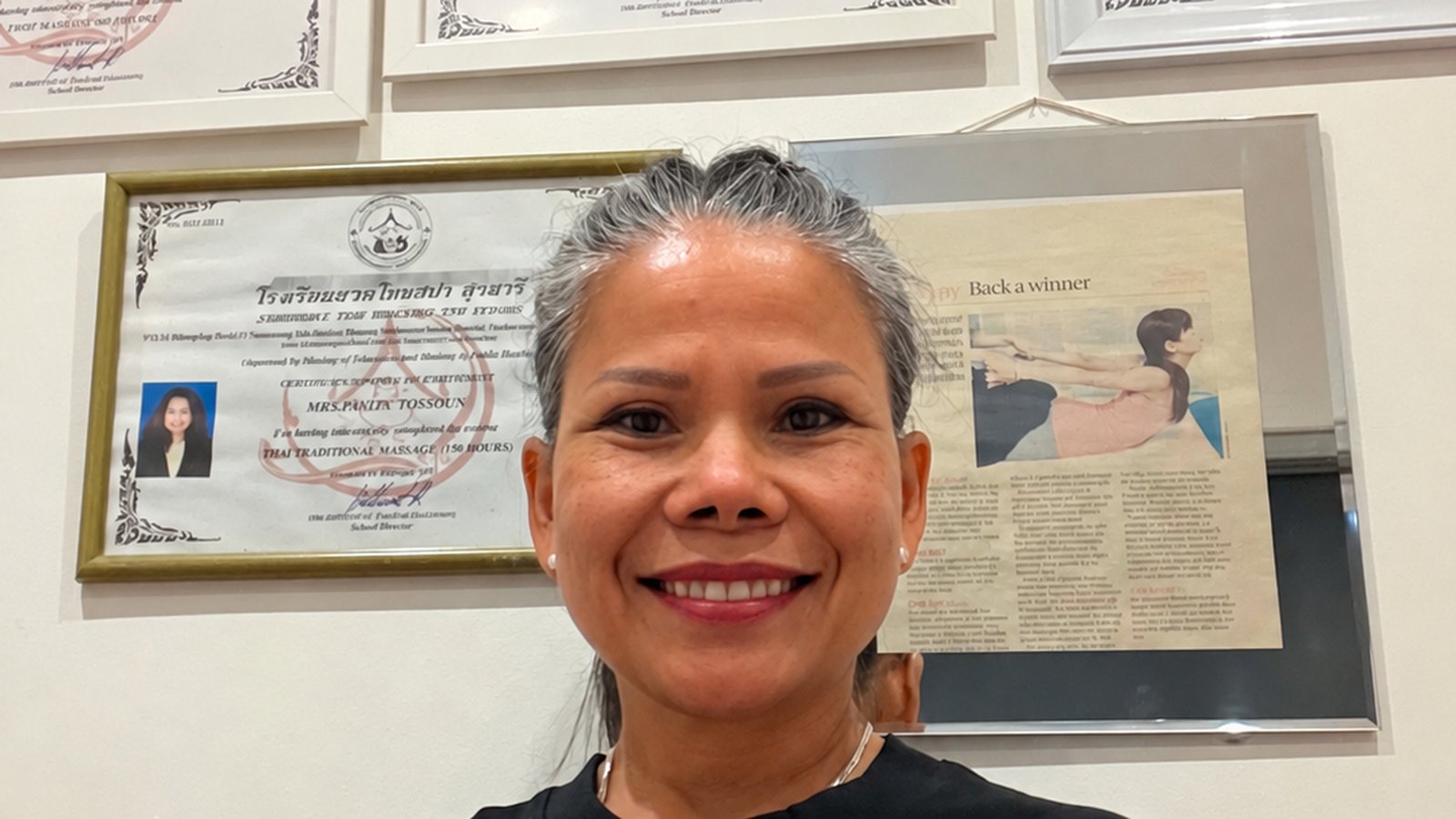 Pailin, owner and therapist at Sabaidee Thai Spa, in front of her framed Thai massage certificates.